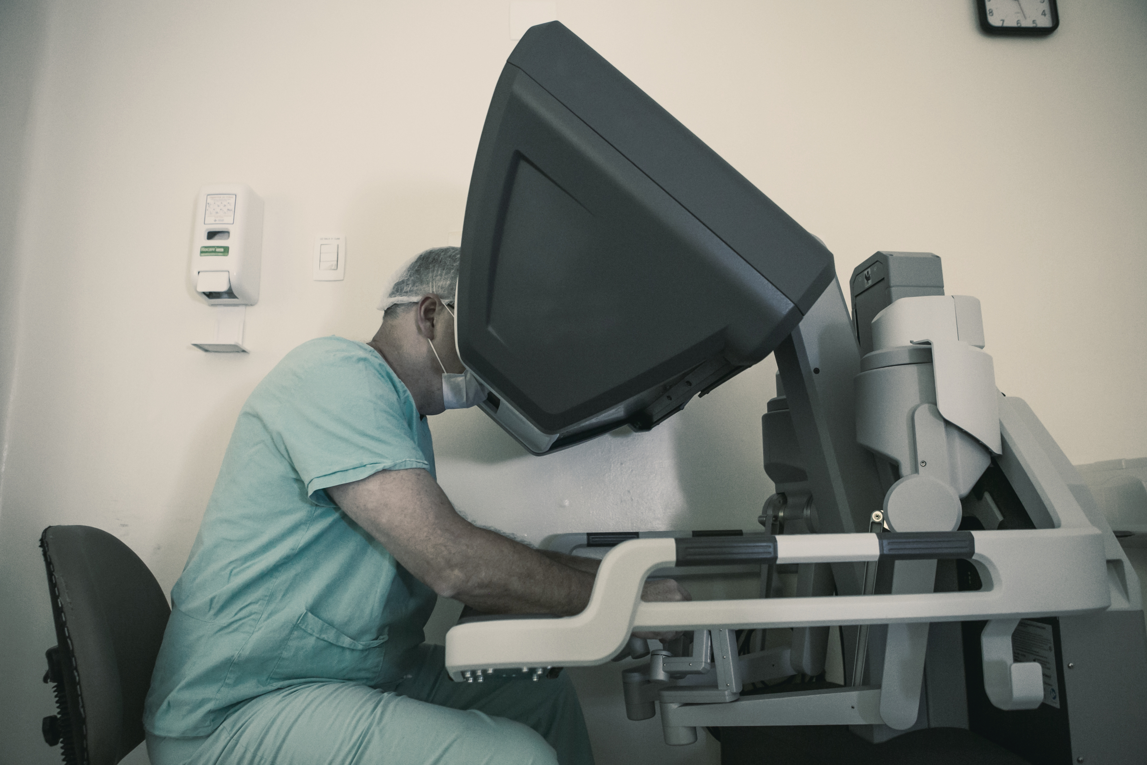 Dr. Fábio Luiz Waechter sentado ao console do robô cirúrgico, operando, com os olhos no visor e as mãos nos controles
