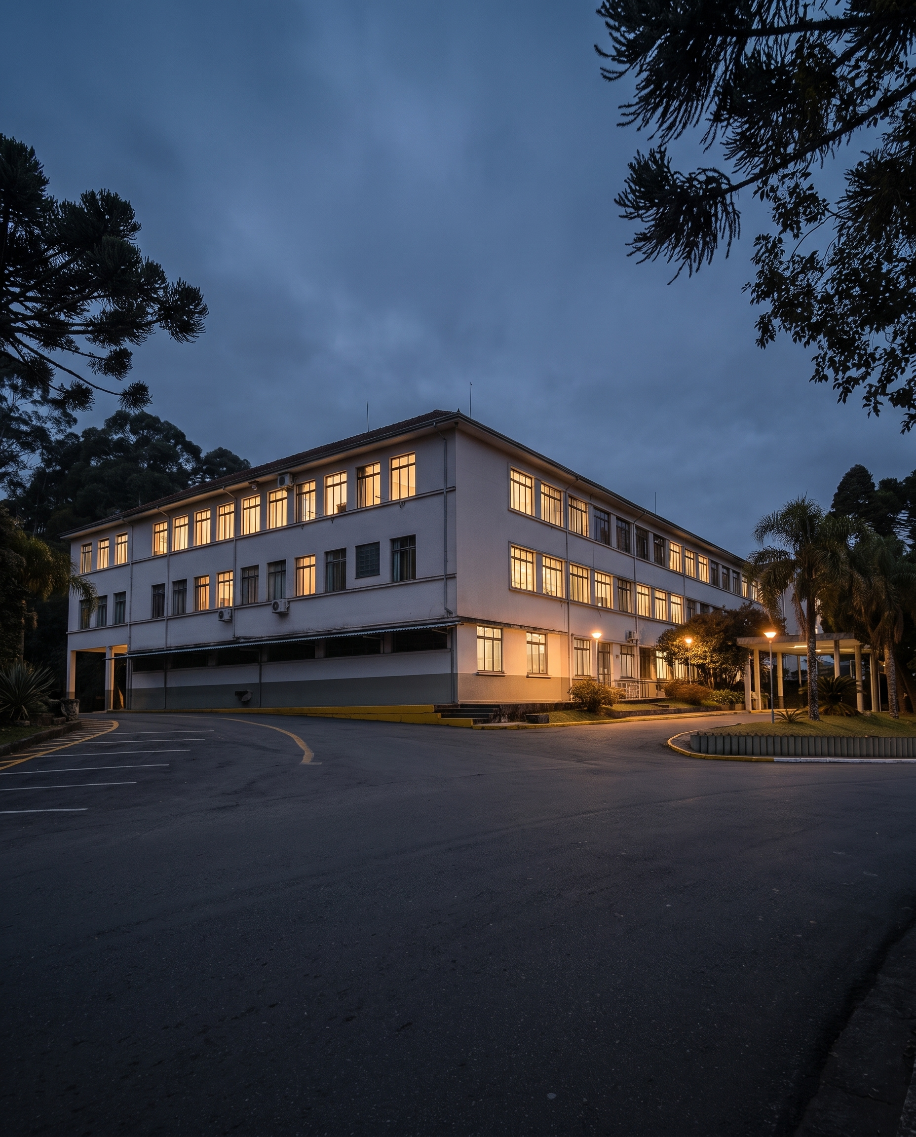 Prédio da reitoria da Universidade de Caxias do Sul ao anoitecer, entre araucárias