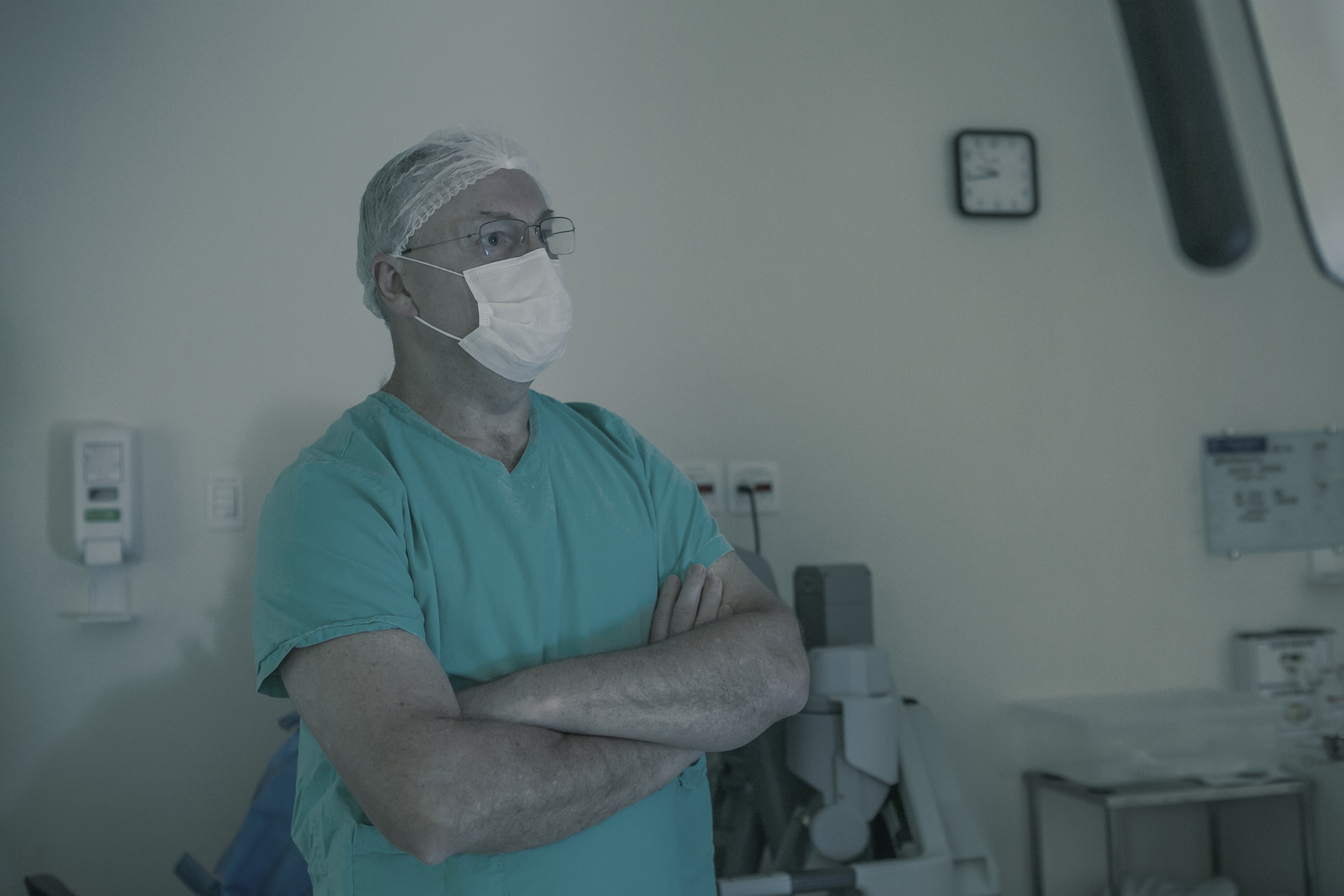 Dr. Fábio Luiz Waechter no bloco cirúrgico, de touca e máscara, ao lado do robô cirúrgico